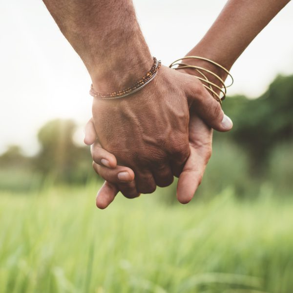 Young couple holding hands in the field Young couple walking through meadow hand in hand. Close up shot with focus on hands of man and woman.