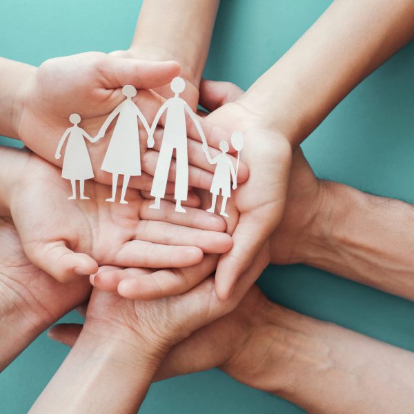 hands holding paper family cutout, family home,adoption foster care, homeless charity, family mental health, homeschooling , household budget during recession concept Adult and children hands holding paper family cutout, family home, foster care, homeless charity support concept, family mental health, international day of families