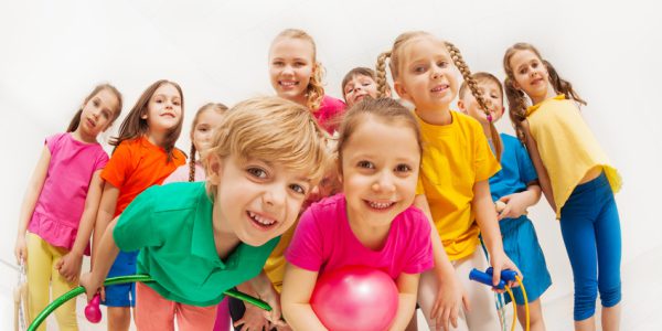Portrait of cute kids in sportswear with female gymnastics coach, holding sports equipment, standing together in gym, looking at camera